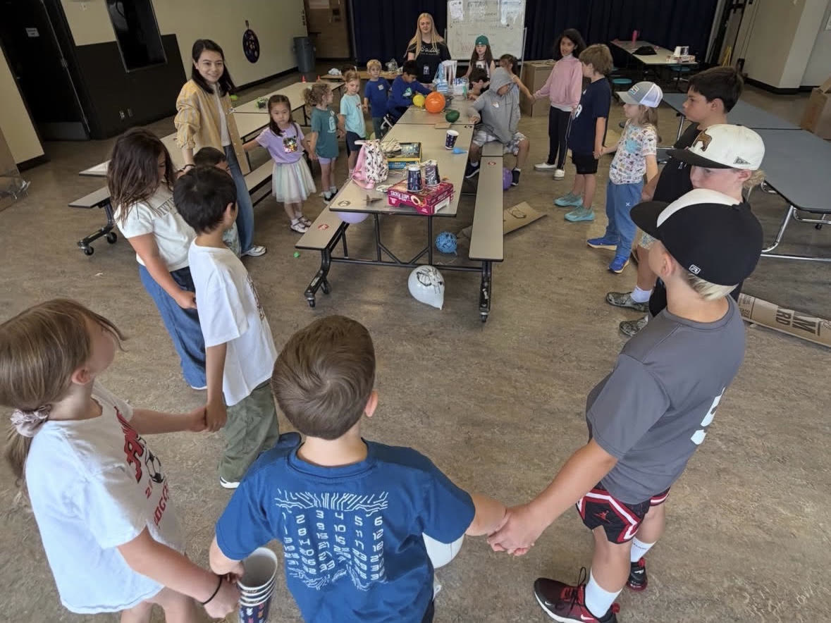 Dr. Tao leading a STEM camp game: students hold hands in a circle around tables of balloons and cups